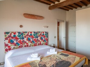 A hotel room with a large bed, a colorful headboard, a wooden ceiling, and a white wardrobe.