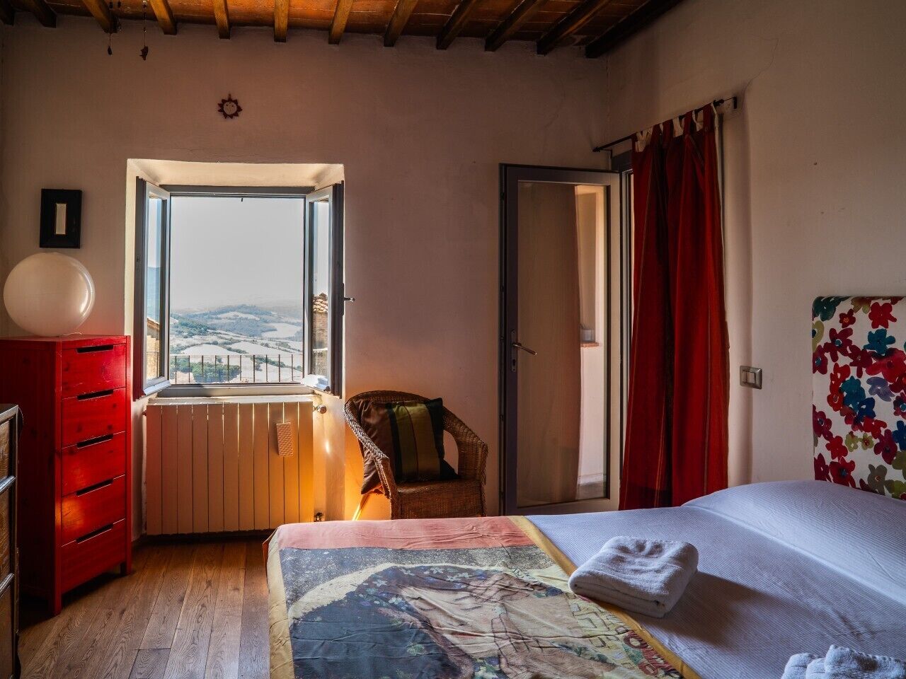 Un dormitorio con una cama, una ventana con vistas, un aparador rojo, una silla y un radiador.
