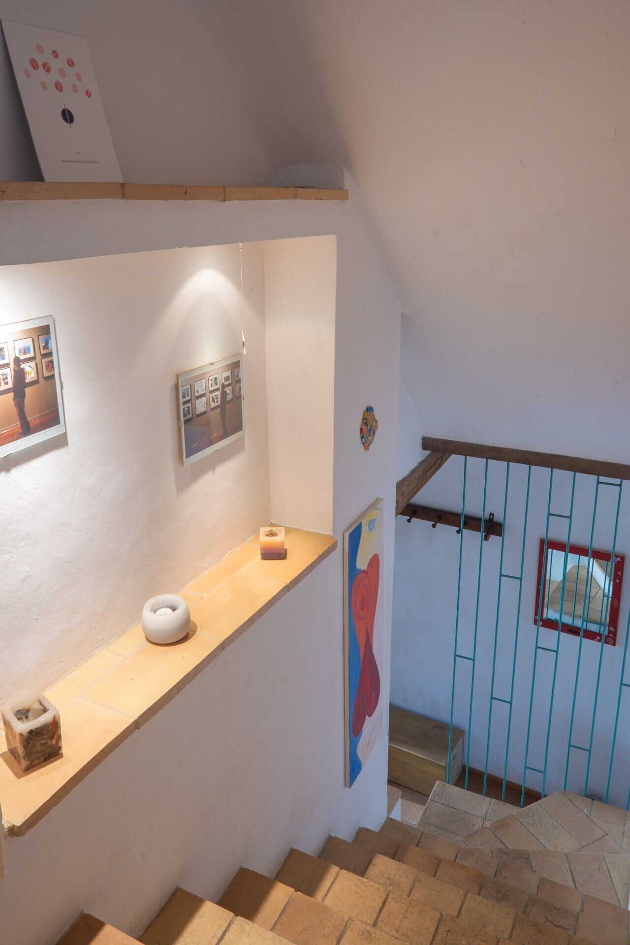 A staircase with a wooden handrail and a blue railing, leading to a landing with a white wall and a framed picture.