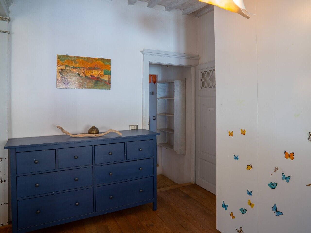 Una habitación con un aparador azul, un cuadro en la pared y una puerta decorada con mariposas.