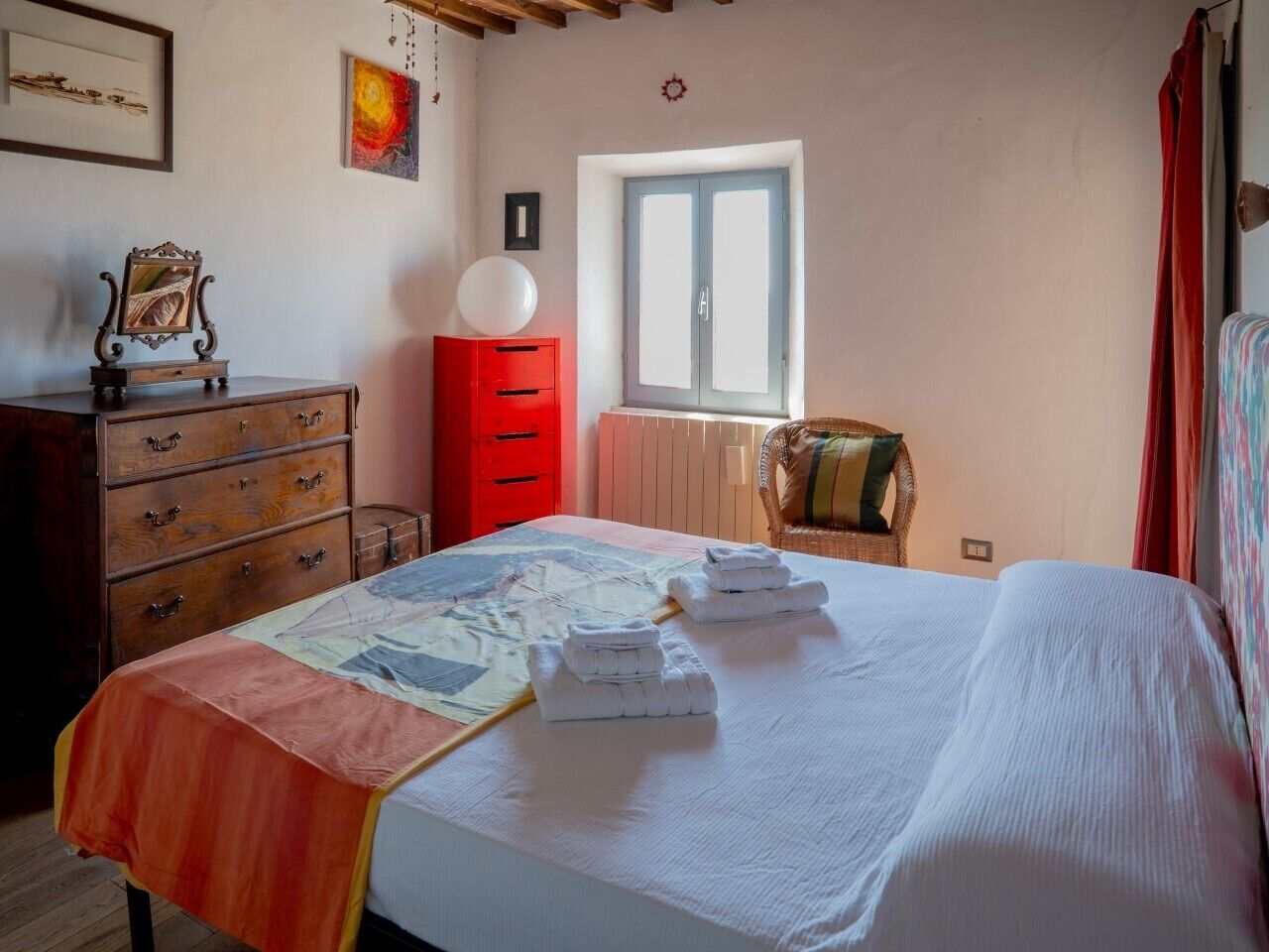 A bedroom with a bed, a dresser, a red cabinet, a window, and a chair.