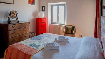 A bedroom with a bed, a dresser, a red cabinet, a window, and a chair.