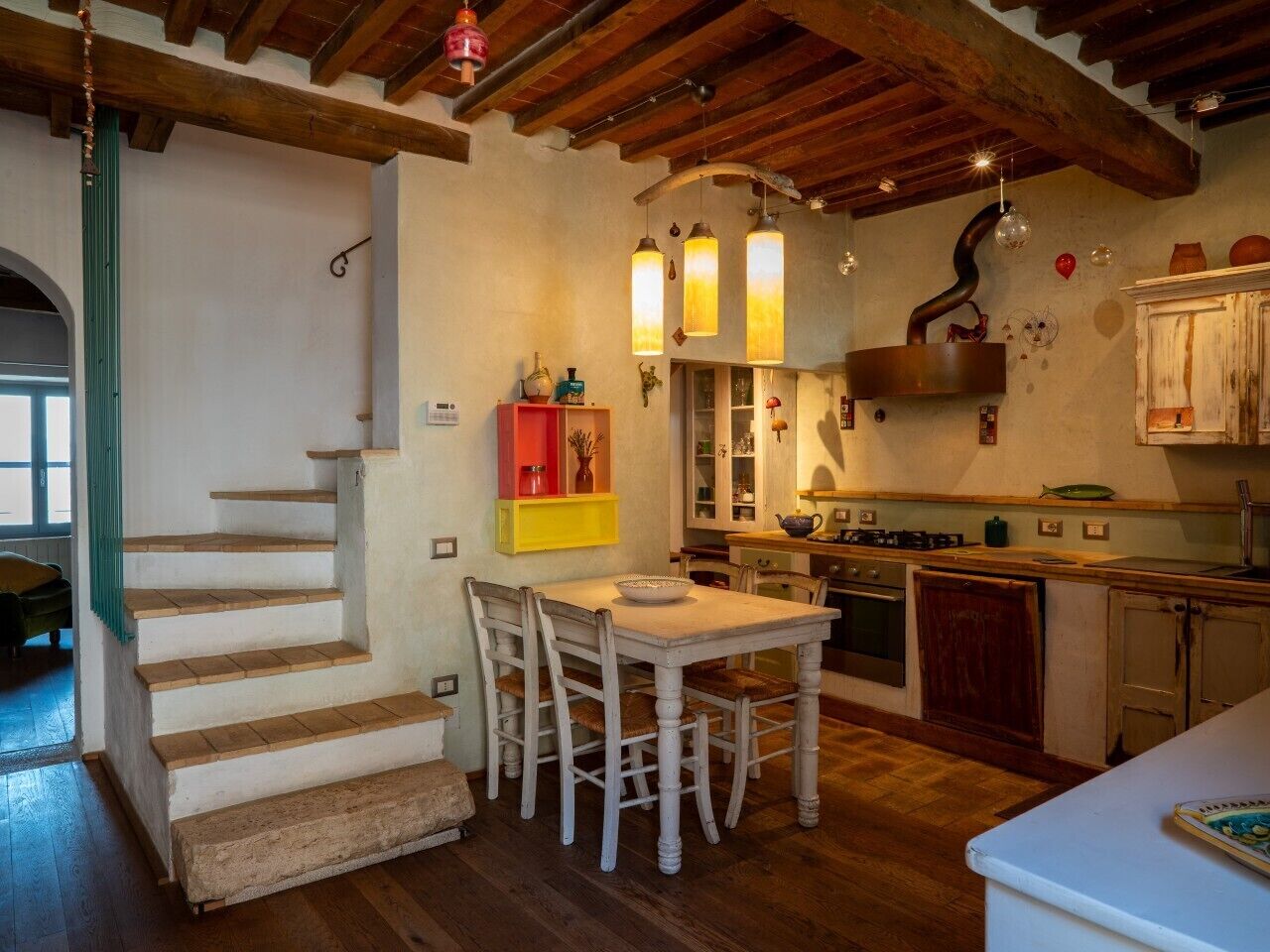 Eine Küche mit Holzboden, einem Esstisch mit Stühlen, einer Treppe und Pendelleuchten.