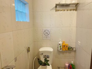 A bathroom with a toilet, a shower, a window with a blue pattern, and a shelf with toiletries. - Peaceful 2BR in the Heart of Hanoi’s Old Quarter | Private Balcony (Hà Nội)