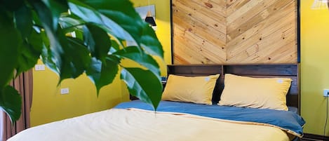 A bed with a wooden headboard, a yellow wall, and a plant in the foreground.