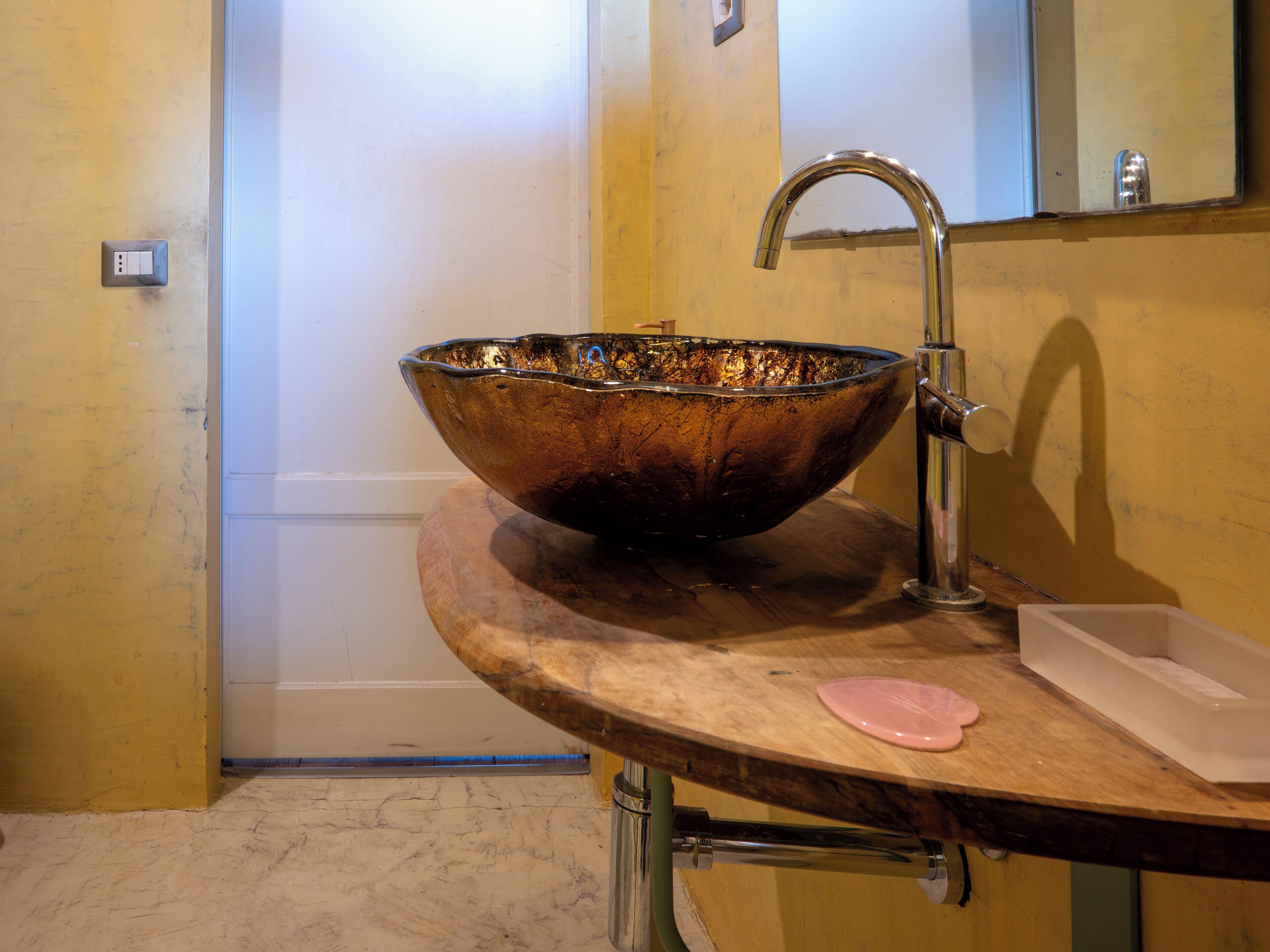 Une salle de bain avec un grand lavabo au design original, un robinet et un miroir au-dessus.