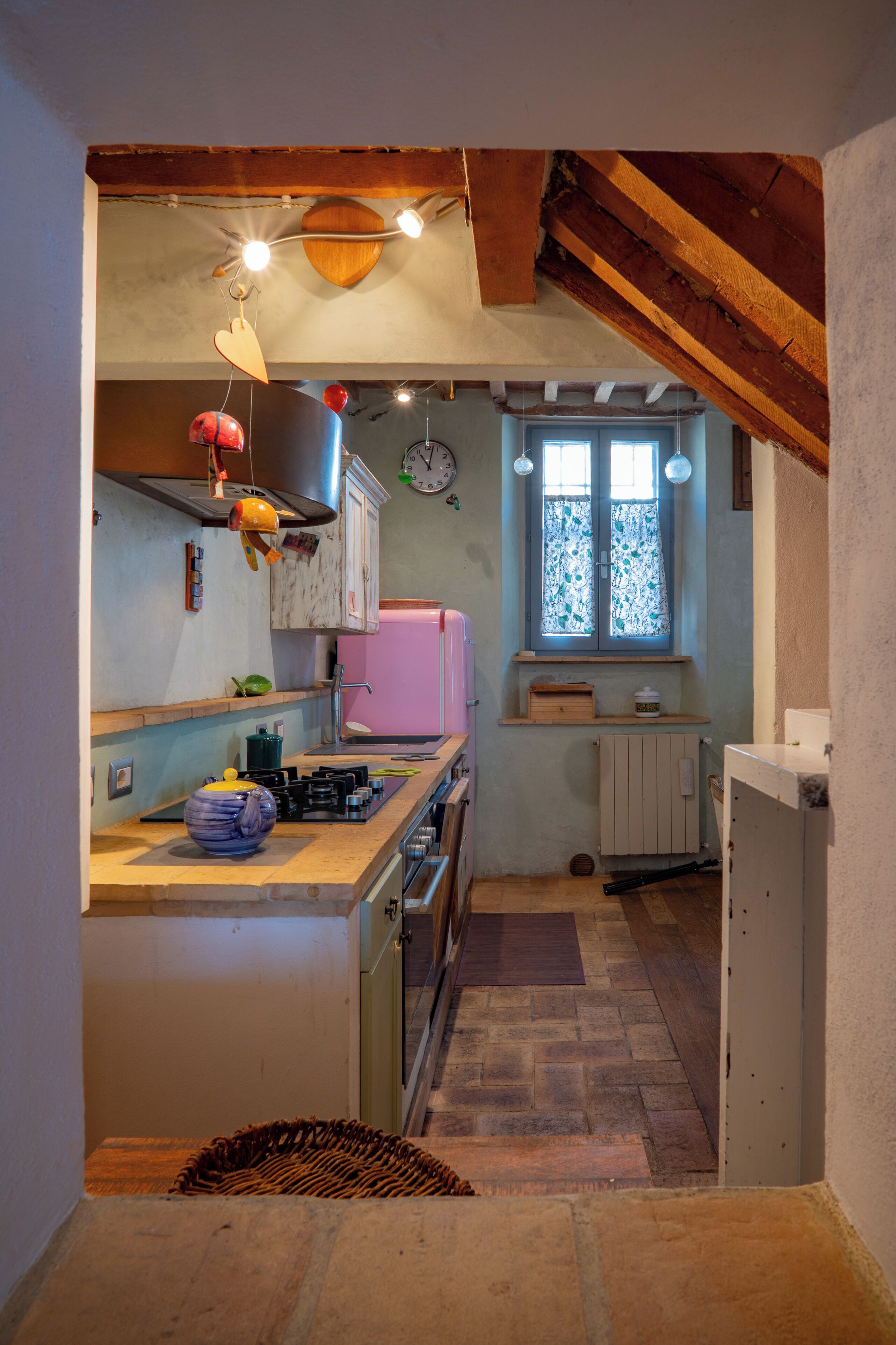A kitchen with a wooden ceiling, a pink refrigerator, and a window with curtains.