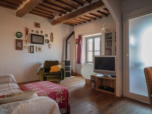 A cozy living room with a green armchair, a flat-screen TV, wooden flooring, and a bookshelf. - Nido con vista (Radicondoli)