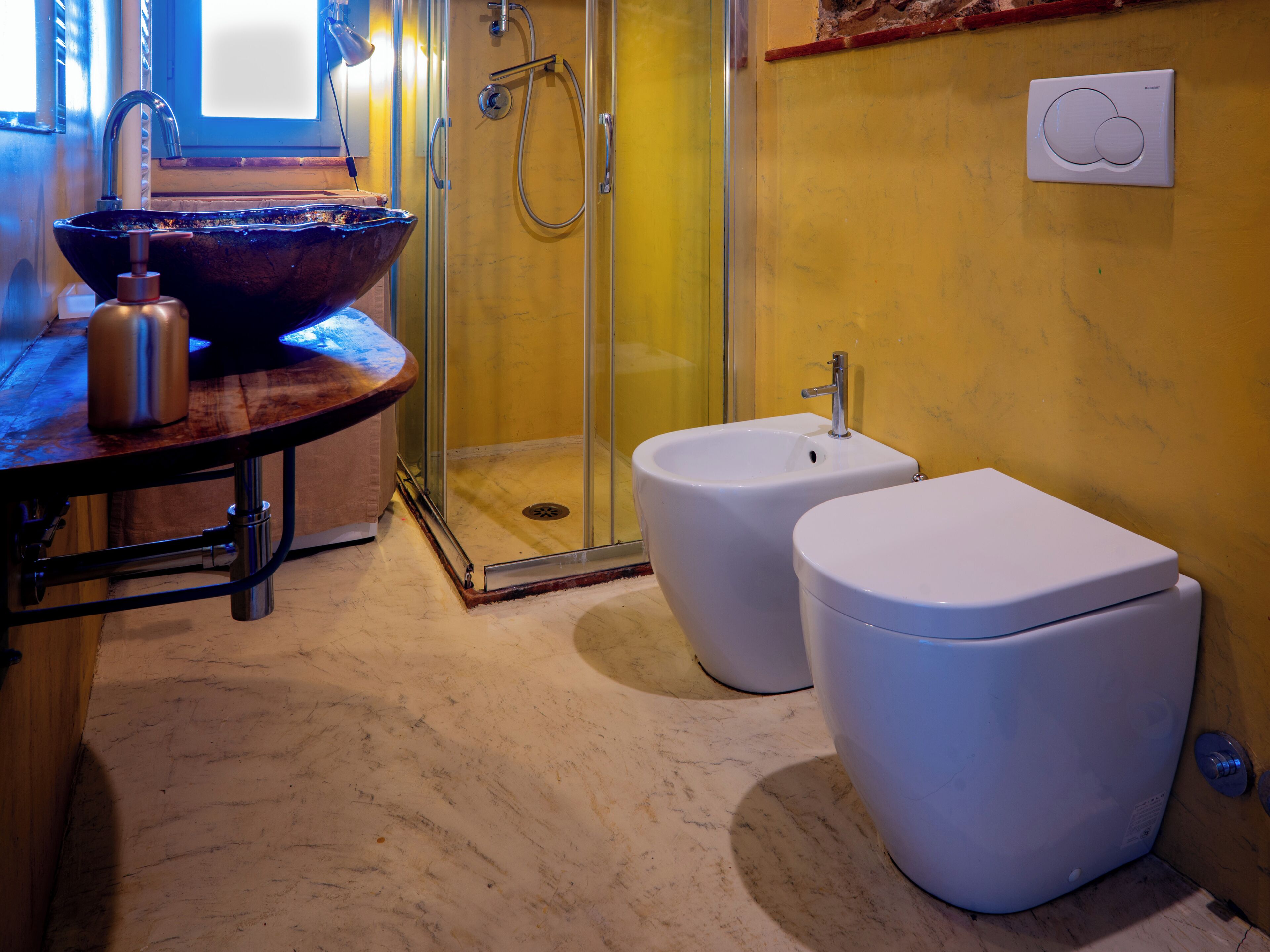 A bathroom with a glass-enclosed shower, a large vessel sink, two bidets, and a toilet.