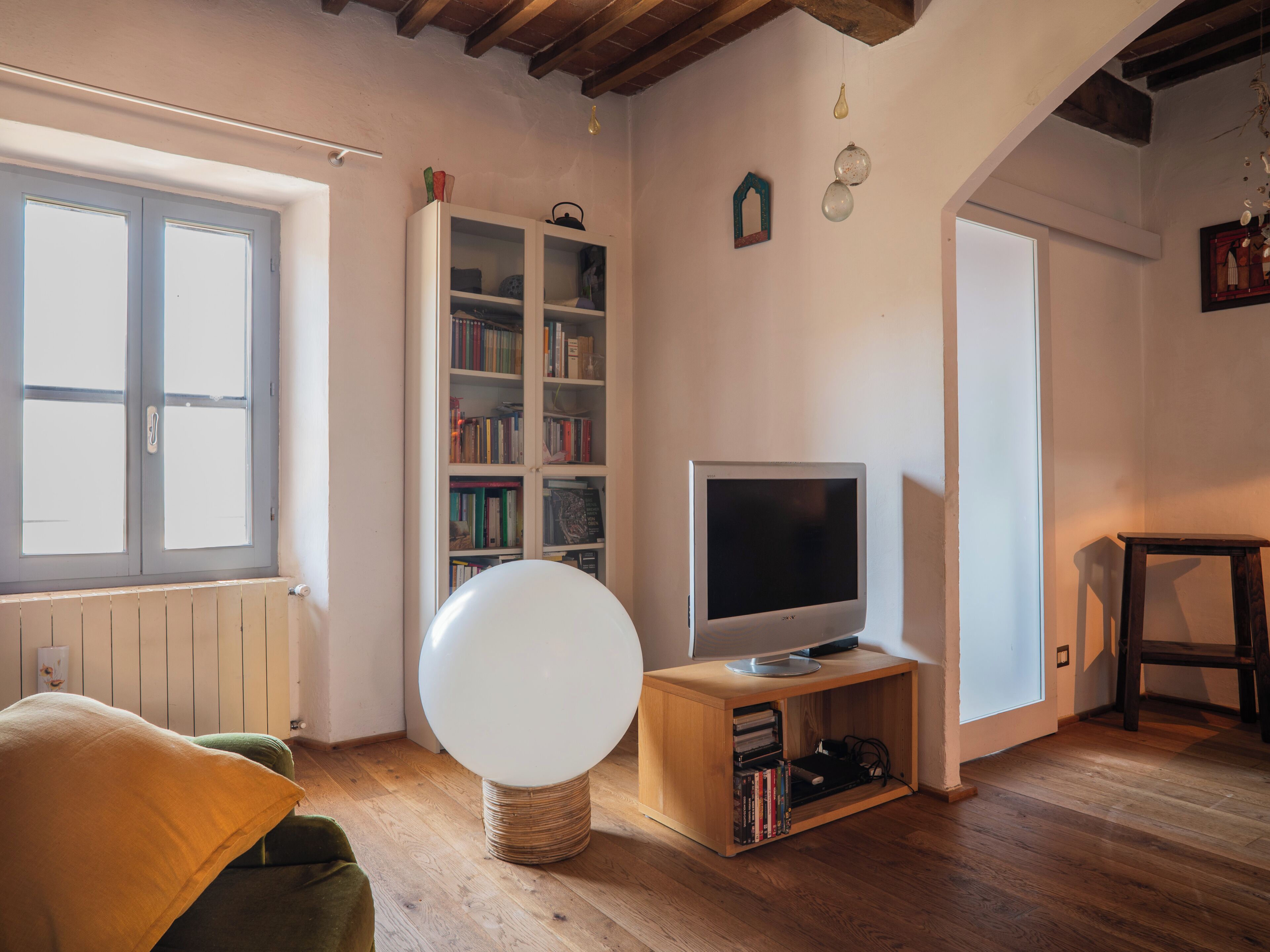 Una habitación con una televisión sobre un mueble de madera, una estantería y una ventana con persianas.
