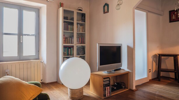 A room with a television on a wooden stand, a bookshelf, and a window with blinds.