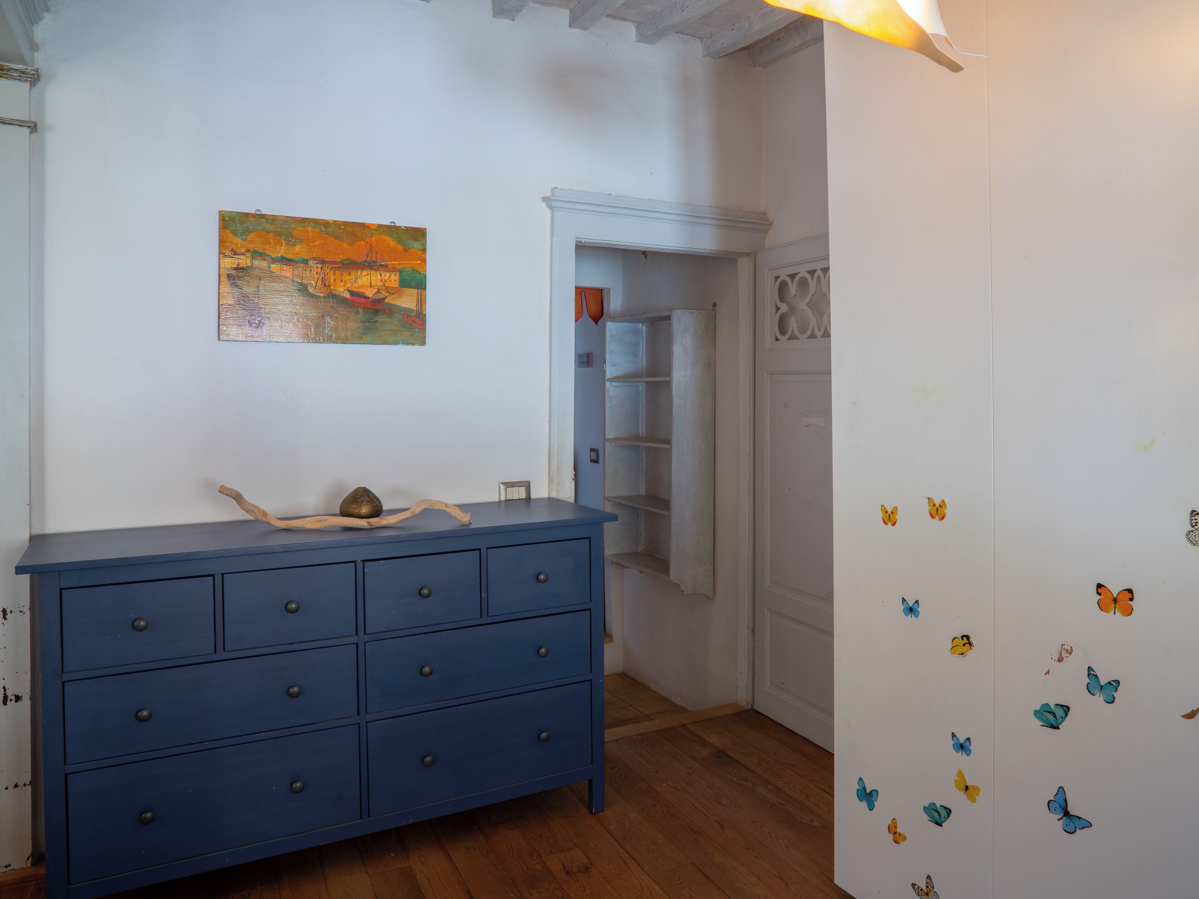 A room with a blue dresser, a painting on the wall, and butterfly decals on the door.
