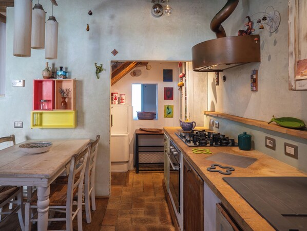 A compact kitchen with a gas stove, a refrigerator, and a wooden dining table with chairs.