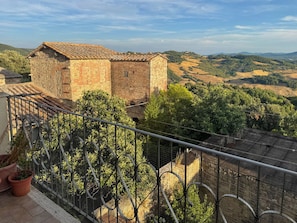 A stone building with a tiled roof, surrounded by lush greenery and hills in the background.