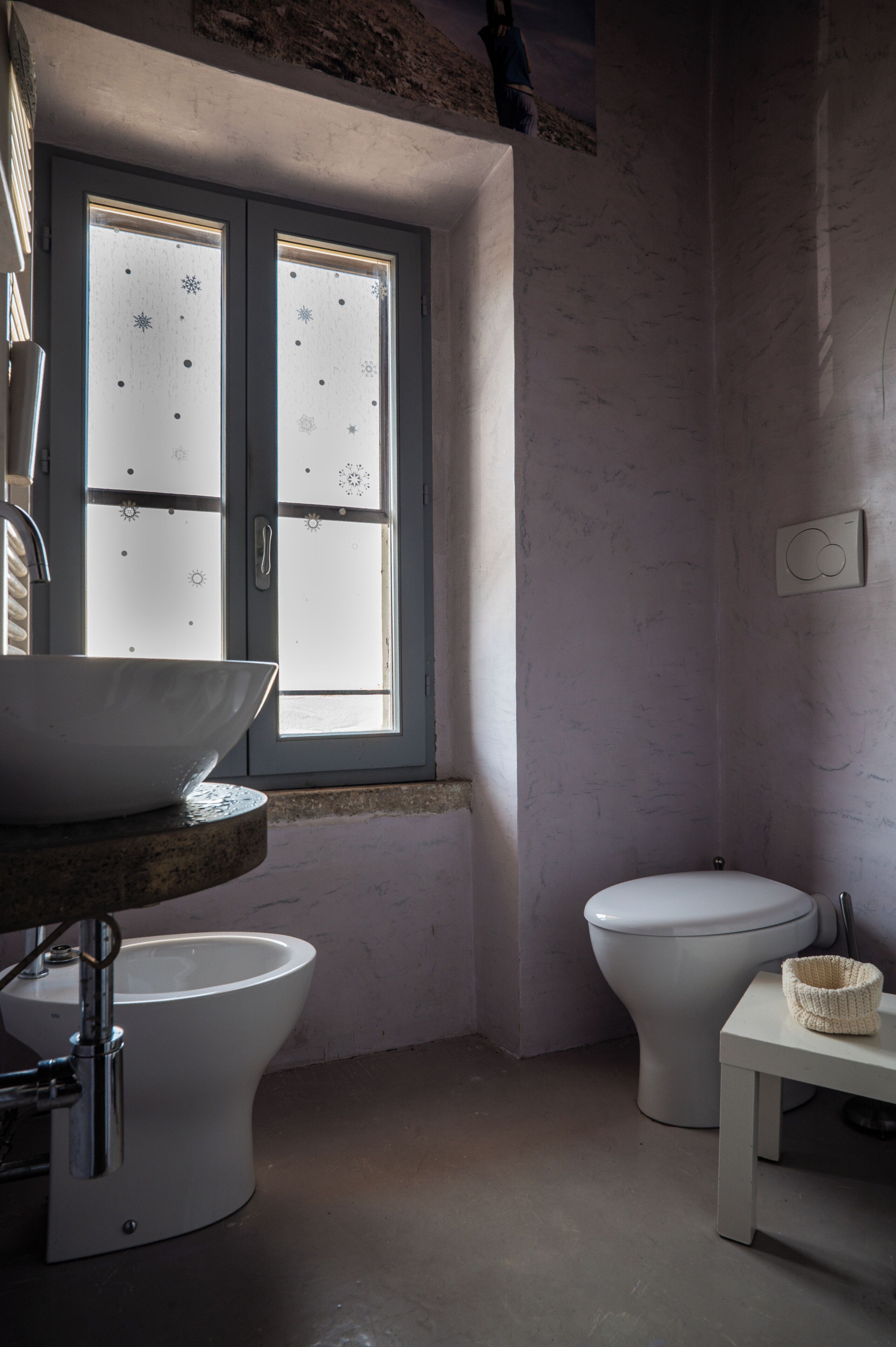 Une salle de bain avec une grande fenêtre, un lavabo, des toilettes et une petite table.
