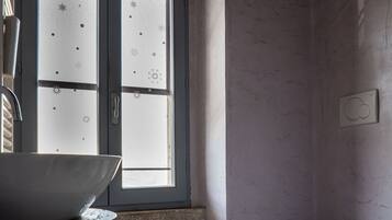 Une salle de bain avec une grande fenêtre, un lavabo, des toilettes et une petite table.