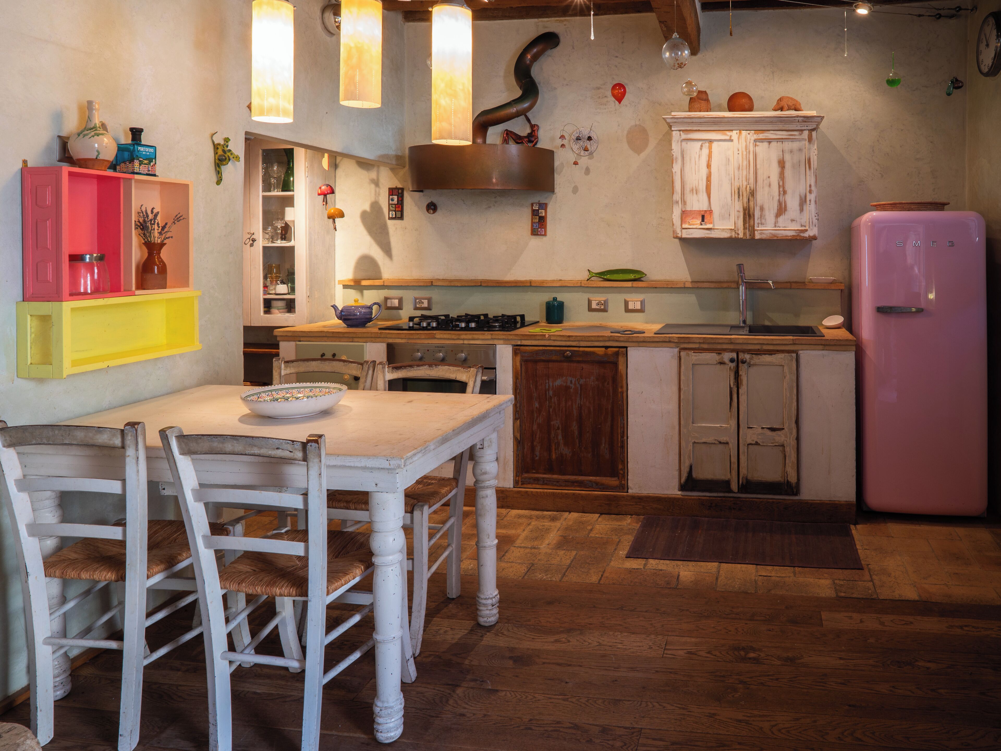Una cocina con una mesa de comedor, sillas, un refrigerador rosa y armarios de madera.