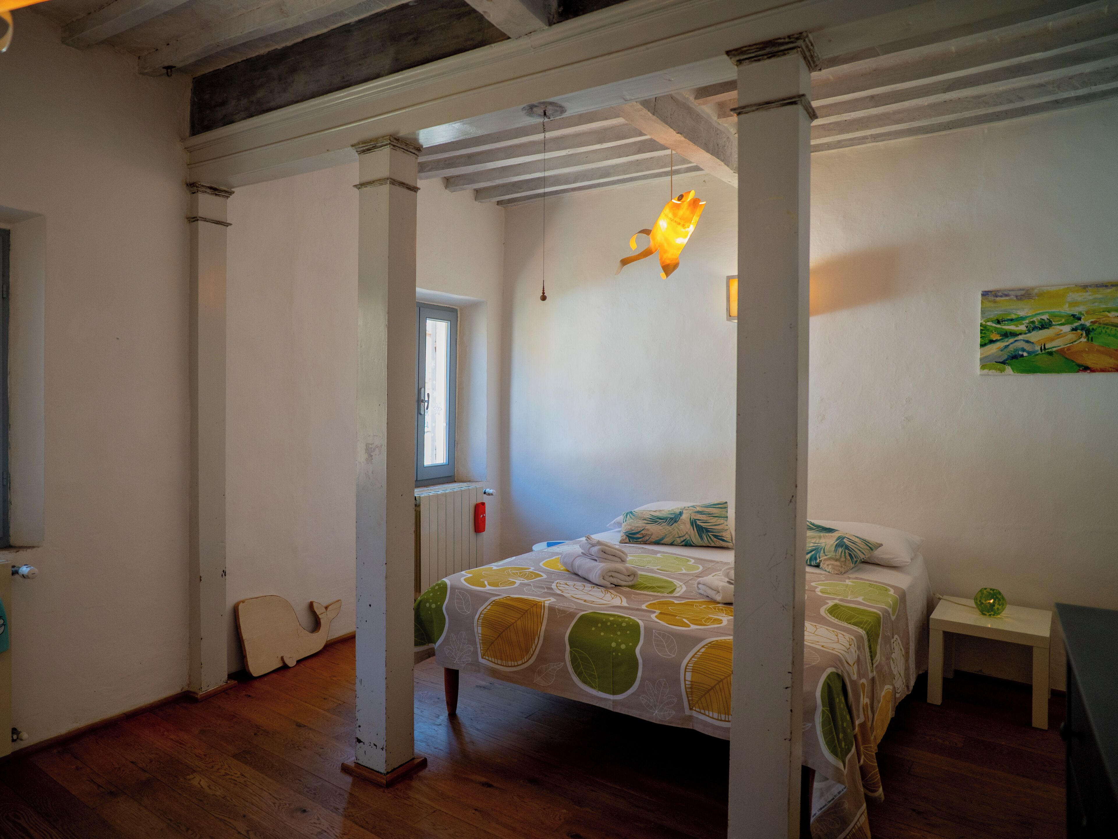 A bedroom with a bed, a nightstand, a window, and a painting on the wall.