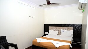 Una habitación de hotel con cama, mesita de noche, silla y ventilador de techo.