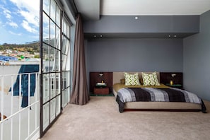 A bedroom with a large window, a bed with patterned bedding, and a view of a cityscape. - Westwood (Cape Town)