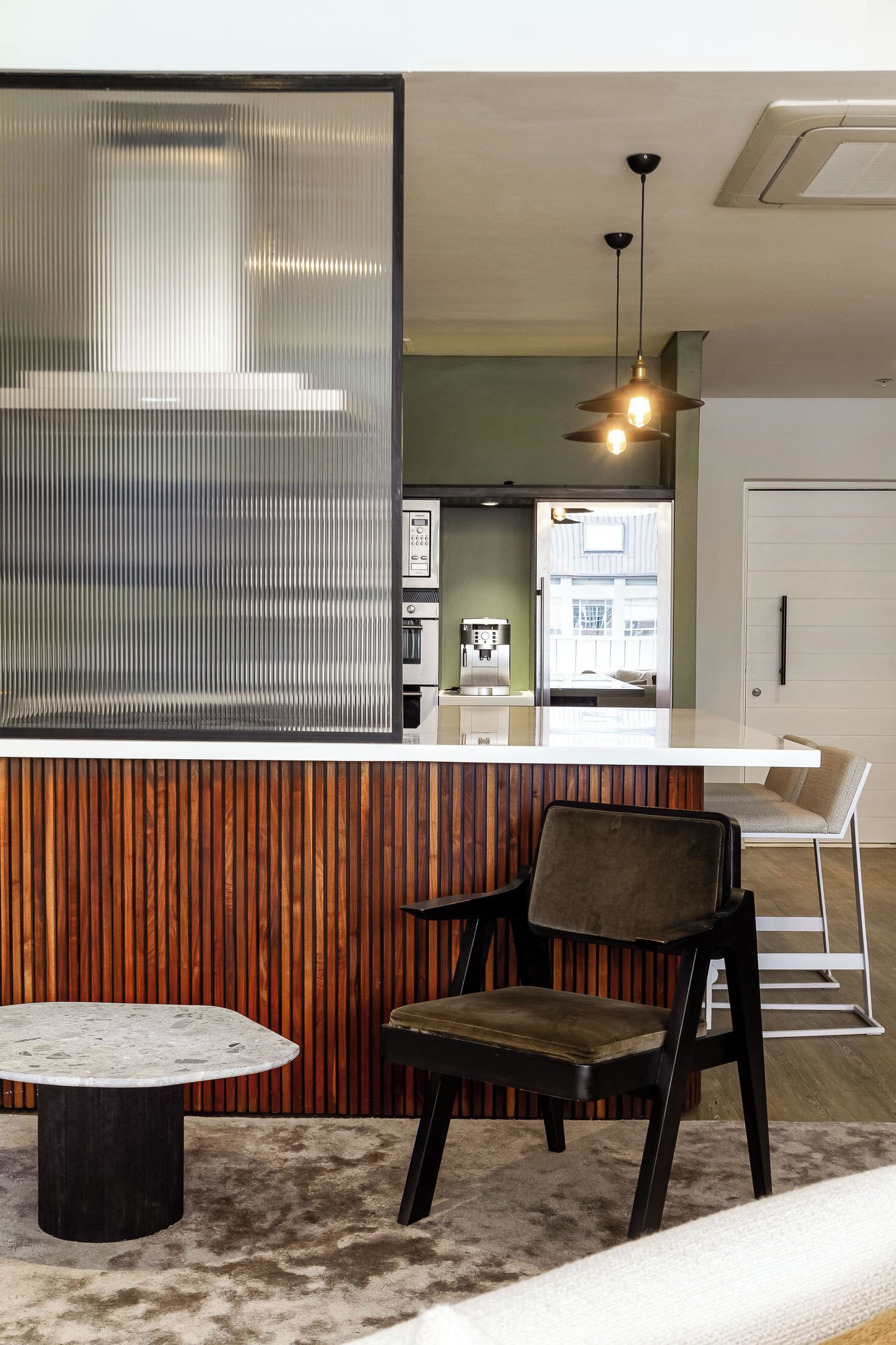 Een moderne keuken met een koffieapparaat, een wand van houten panelen en een zithoek met een tafel en stoelen.