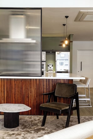 A modern kitchen with a coffee machine, a wooden panel wall, and a seating area with a table and chairs. - Westwood (Cape Town)