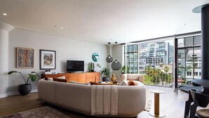 Uma sala de estar moderna com um sofá grande, uma televisão de tela plana e uma área de jantar com mesa e cadeiras.