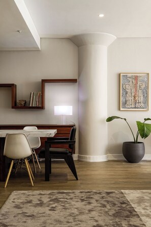 Un espace repas moderne avec une table en bois, des chaises, une grande plante en pot et un tableau abstrait encadré accroché au mur.