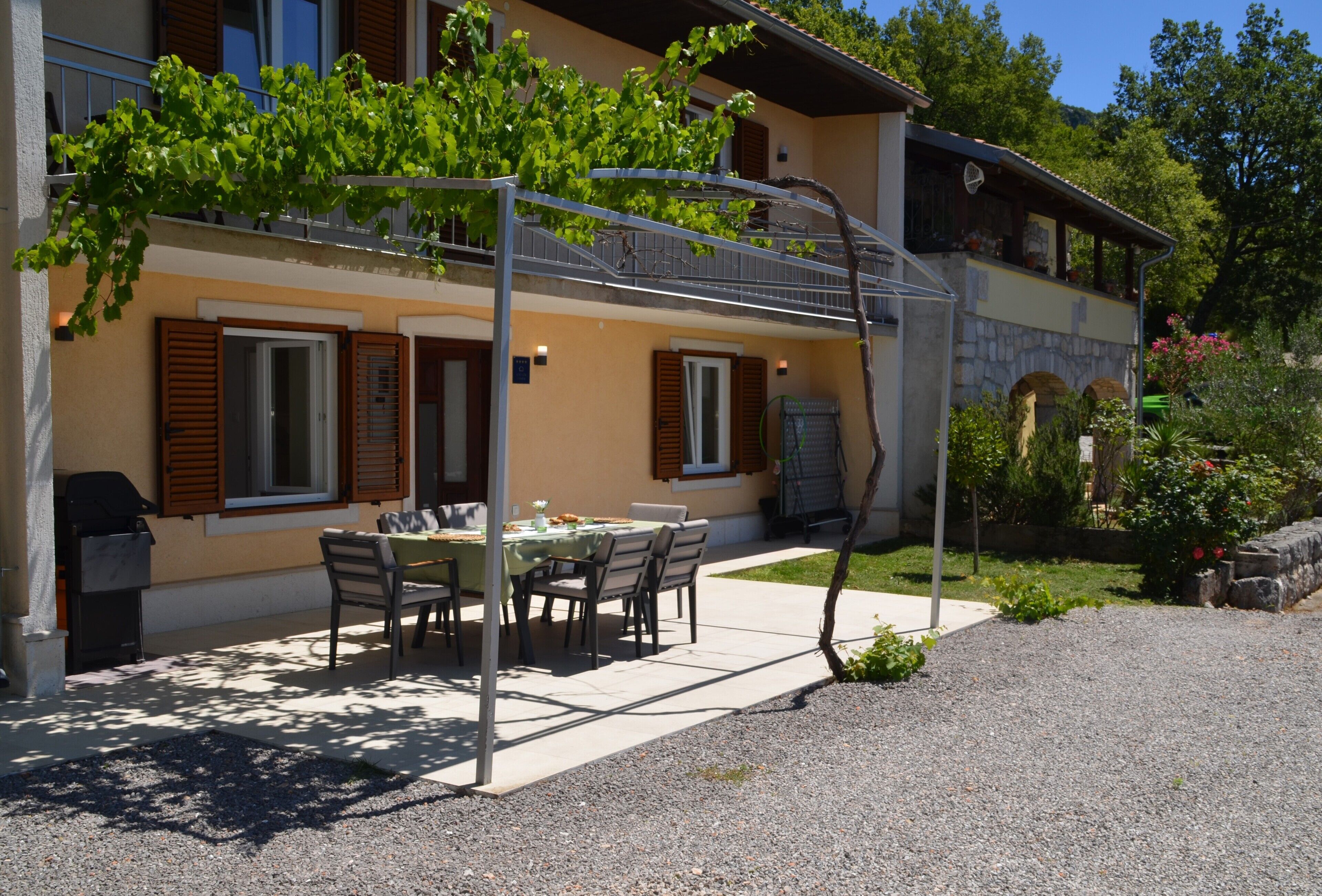 Ein Gebäude mit einer überdachten Außenessbereich, einer Pergola mit Kletterpflanzen und einer Steinmauer.