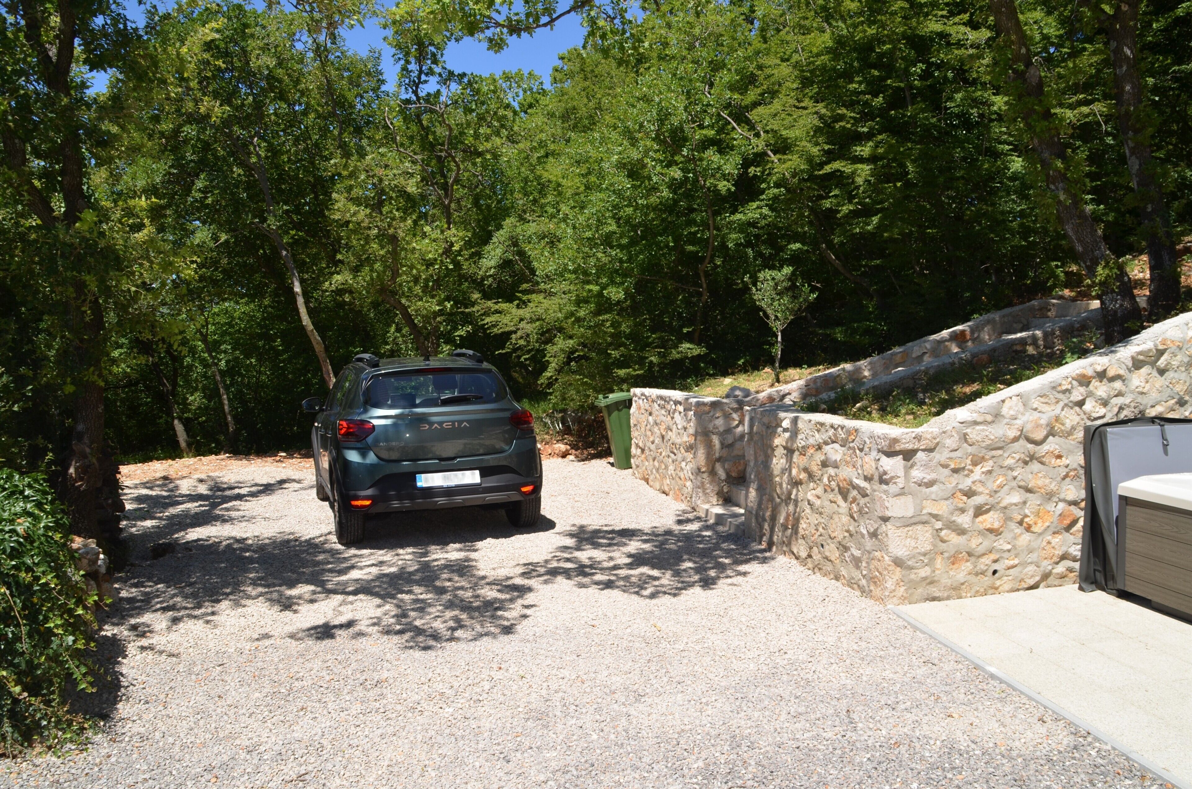 A vehicle parked on a gravel path with a stone wall and trees in the background.