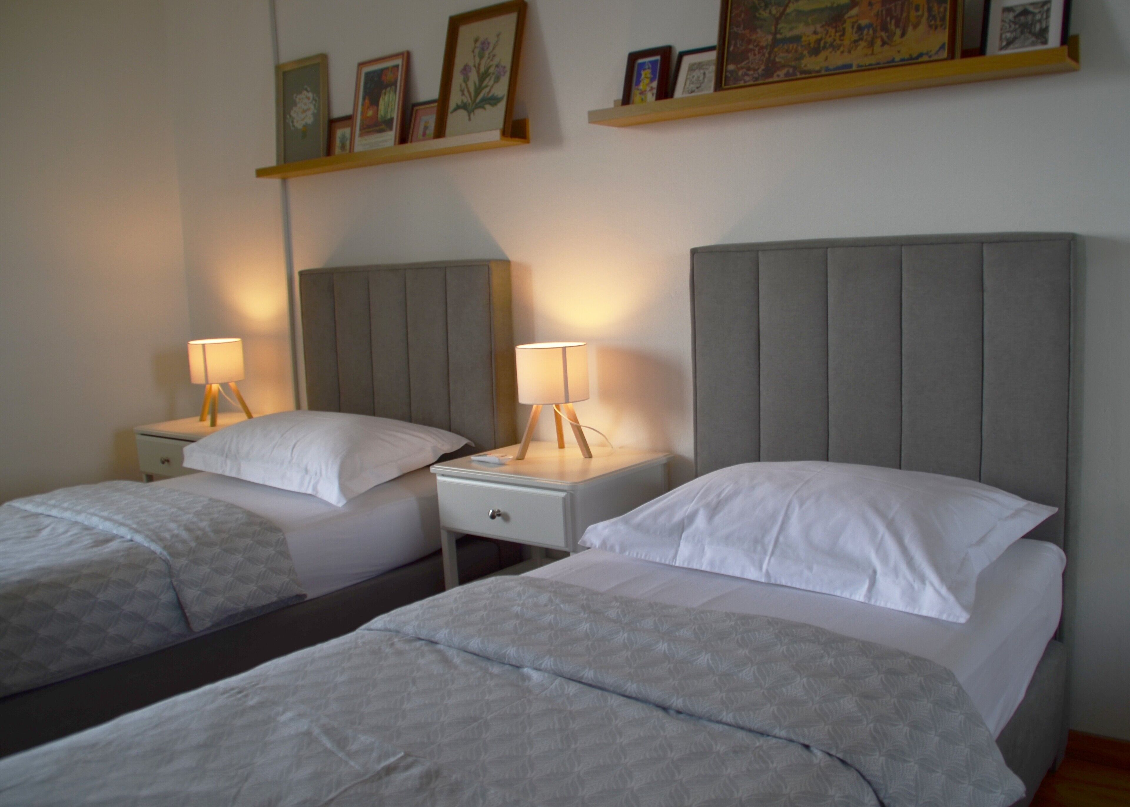 Ein Hotelzimmer mit zwei Betten, Nachttischen, Lampen und einem Regal mit gerahmten Bildern.