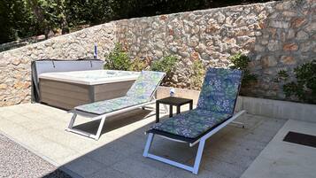 A stone wall, two lounge chairs, and a hot tub in an outdoor setting.