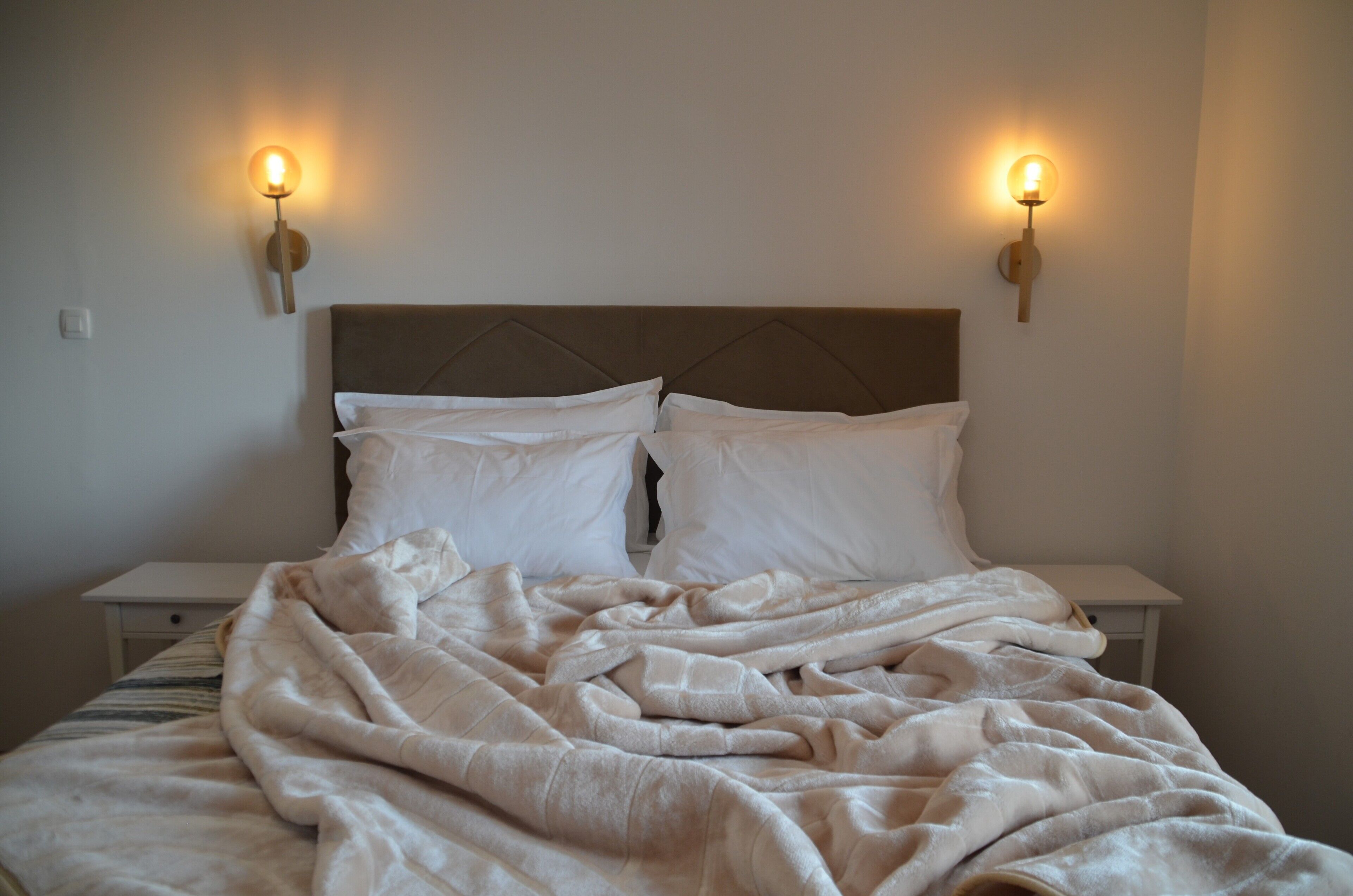 A bed with a headboard, two bedside lamps, and a blanket.