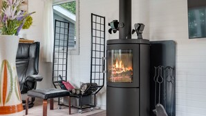 Ett mysigt rum med en vedeldad kamin, en bekväm fåtölj och ett litet bord med en vas med blommor.