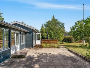 Ein Wohnhaus mit gepflasterter Auffahrt, einer Holzbank und einem Garten.