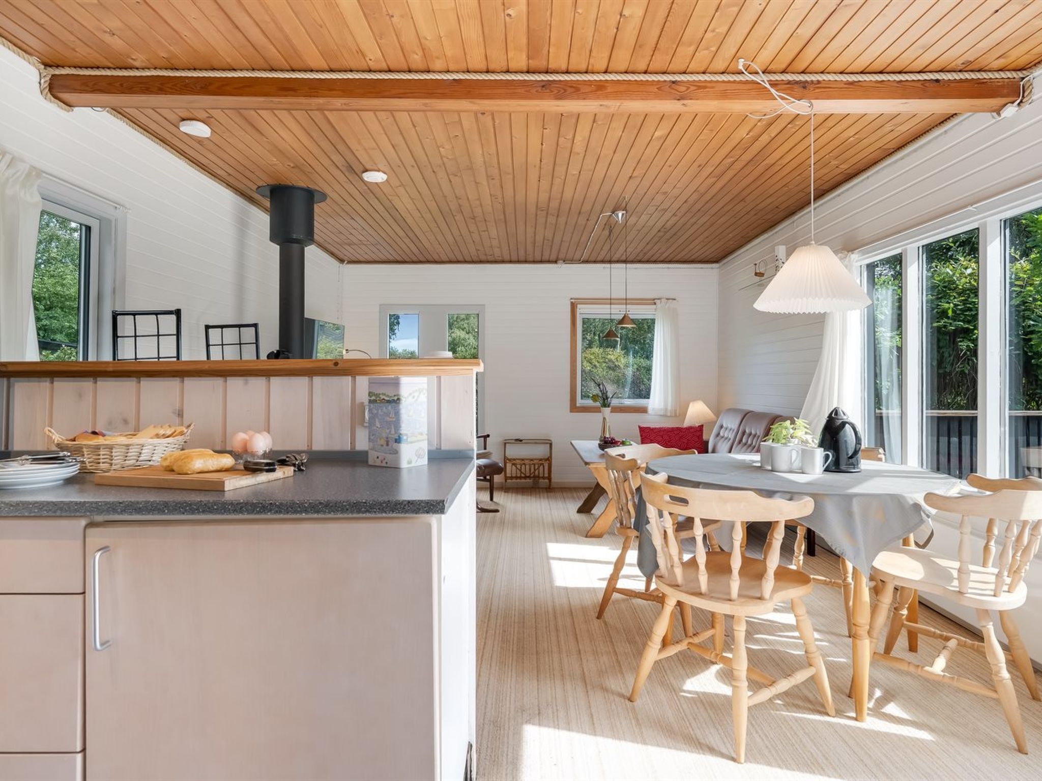 A modern kitchen with a central island, wooden ceiling, and large windows.