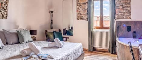 A bedroom with a bed, a bedside table, a mirror, a window with curtains, and a stone wall.