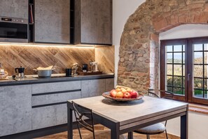 Una cocina moderna con pared de piedra, zona de comedor con una mesa para dos personas, y vista por una ventana.