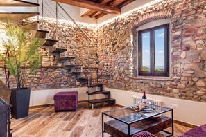 Un intérieur moderne avec un mur en pierre, un escalier en bois, une table en verre et une vue par la fenêtre.