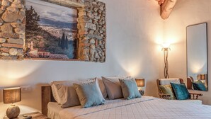 A bedroom with a bed, bedside lamps, a nightstand, a dresser, a mirror, and a stone wall with a scenic painting. - Luxury Chianti Road - 3BR Free Parking (San Casciano in Val di Pesa)