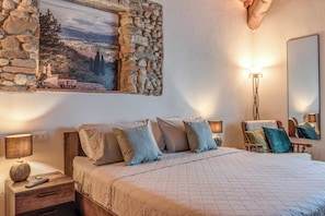 A bedroom with a bed, bedside lamps, a nightstand, a dresser, a mirror, and a stone wall with a scenic painting. - Luxury Chianti Road - 3BR Free Parking (San Casciano in Val di Pesa)
