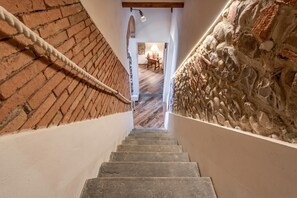A staircase with a brick wall on one side and a stone wall on the other, leading to a room with a wooden table and a lamp. - Luxury Chianti Road - 3BR Free Parking (San Casciano in Val di Pesa)