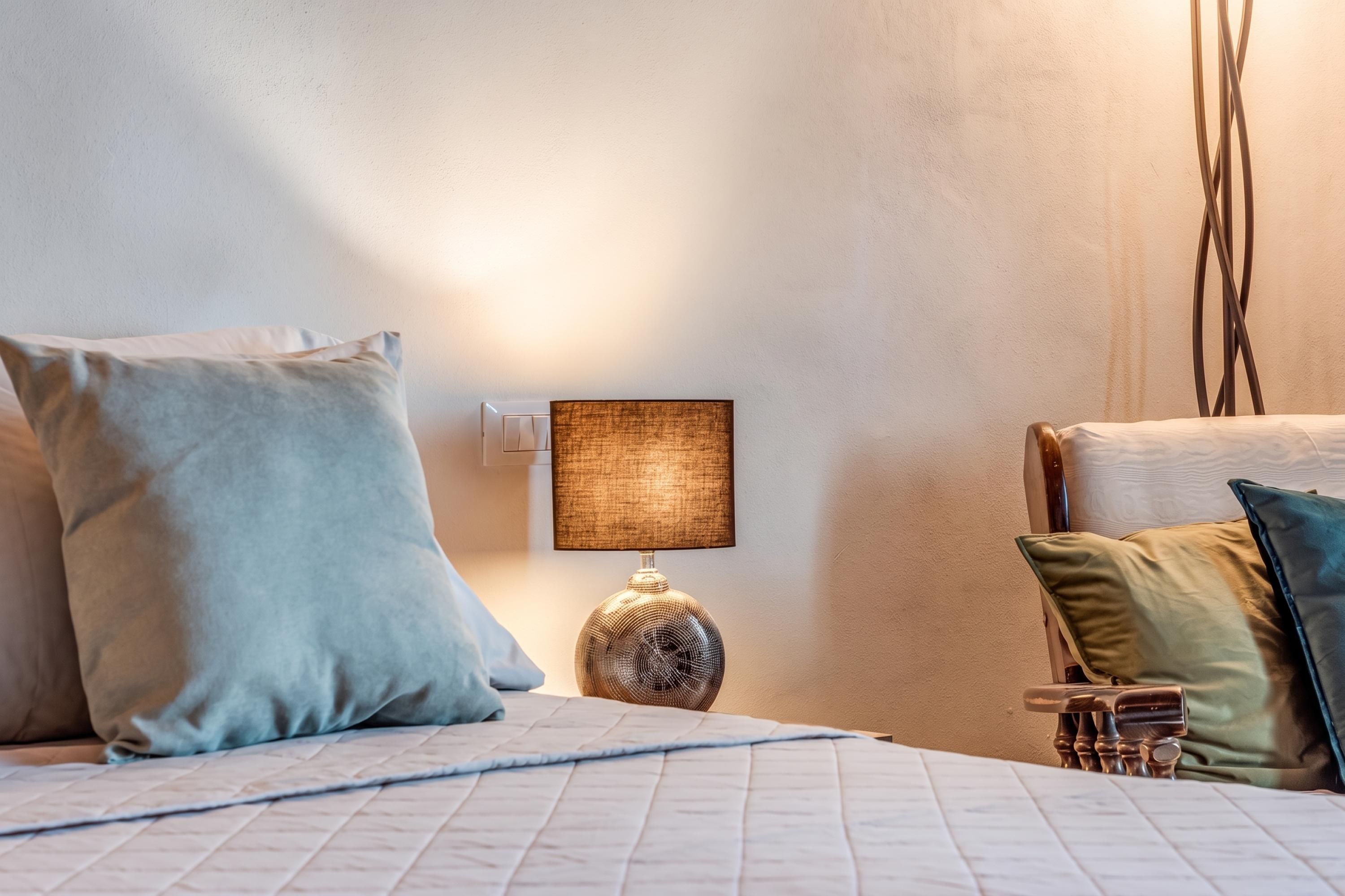Una cama bien tendida con una colcha acolchada, una lámpara de noche y varias almohadas.