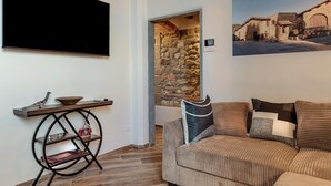 A living room with a flat-screen TV, a stone wall, a sofa with cushions, and a framed picture on the wall. - Luxury Chianti Road - 3BR Free Parking (San Casciano in Val di Pesa)