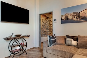 A living room with a flat-screen TV, a stone wall, a sofa with cushions, and a framed picture on the wall. - Luxury Chianti Road - 3BR Free Parking (San Casciano in Val di Pesa)