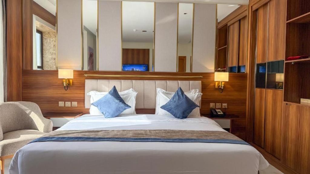 A hotel room with a large bed, two bedside lamps, a wooden headboard, and a wardrobe.