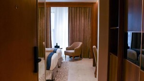 A hotel room with a bed, a chair, a desk, and a large window with curtains.