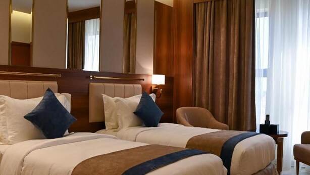 A hotel room with two beds, a sitting area, and a view of the outdoors. - Corp Yanbu Hotel B2 (Yanbu)