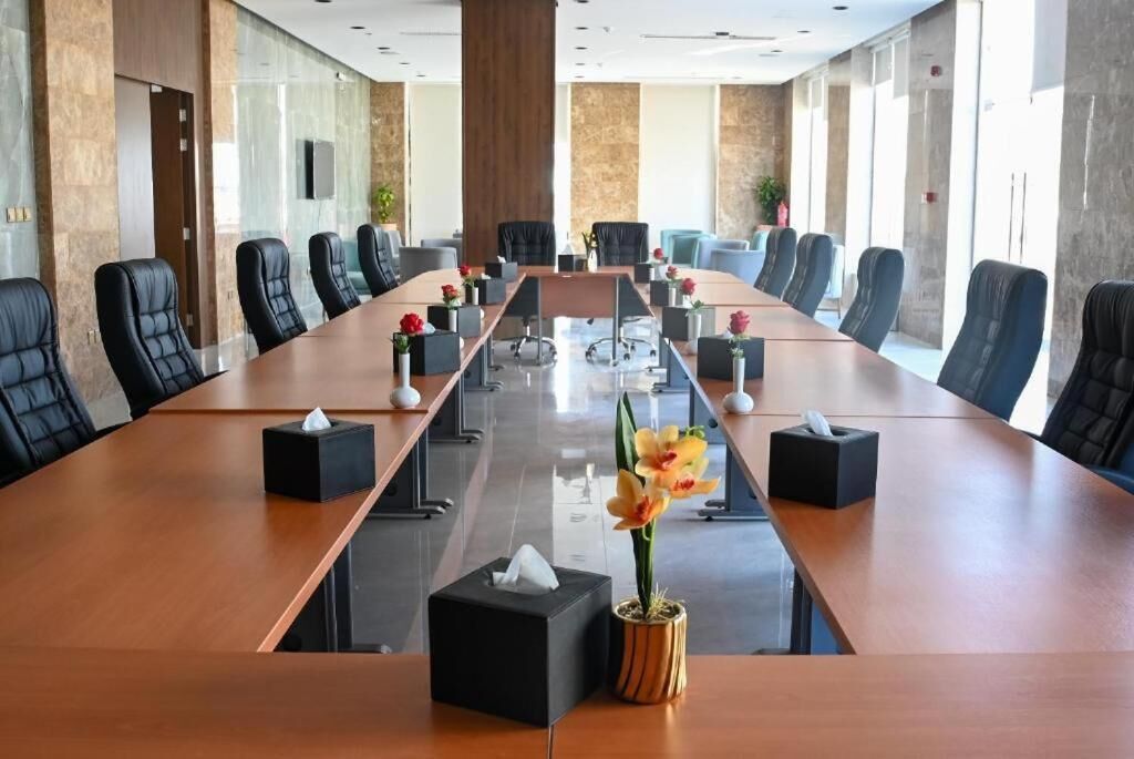 Une salle de conférence avec une longue table, des chaises noires et une plante en pot.
