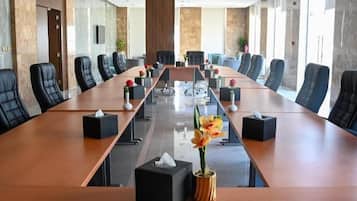 Une salle de conférence avec une longue table, des chaises noires et une plante en pot.